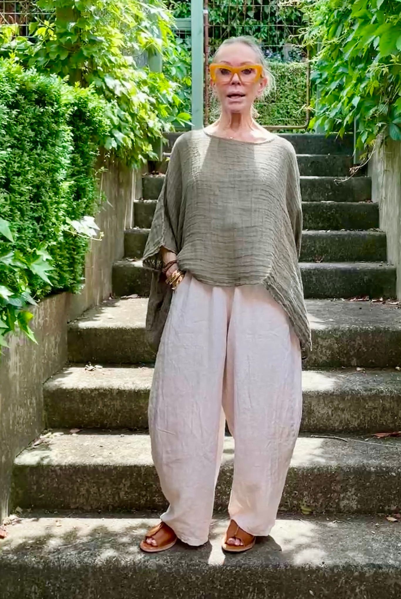 Person standing on outdoor steps wearing a green top and white pants.
