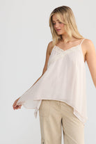 A woman modeling a light cream camisole top and beige cargo pants against a plain light gray studio background.